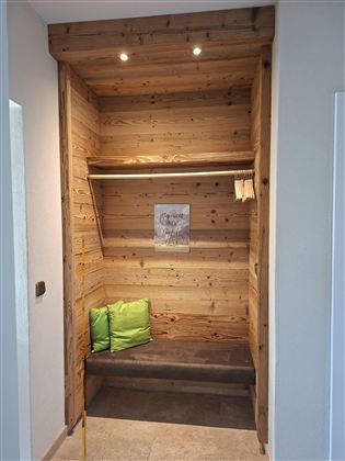 A cozy entrance area with wooden shelves and a bench. Two green cushions provide additional comfort.