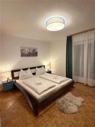 Ein gemütliches Schlafzimmer mit einem Doppelbett und zwei Nachttischen. Sanfte Beleuchtung und ein großes Fenster sorgen für eine einladende Atmosphäre.