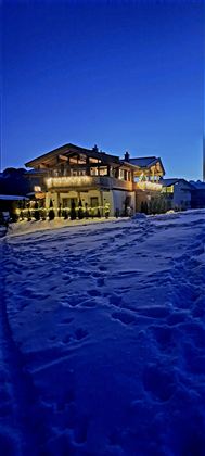 Ein schönes Holzhaus mit warmem Licht in einer verschneiten Landschaft. Der Himmel ist dunkelblau und es gibt frischen Schnee rund um das Haus.