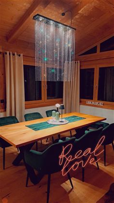 Ein modernes Esszimmer mit einem langen Holztisch und stilvollen grünen Stühlen. Über dem Tisch hängt eine auffällige hängende Lampe mit Ketten.