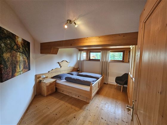 Ein gemütliches Schlafzimmer mit einem Doppelbett und Holzfußboden. Es gibt ein Fenster mit Blick ins Freie und ein Bild an der Wand.