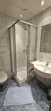 Ein modernes Badezimmer mit einer Duschkabine und einem Waschbecken. Der Boden ist mit grauen Fliesen ausgelegt.