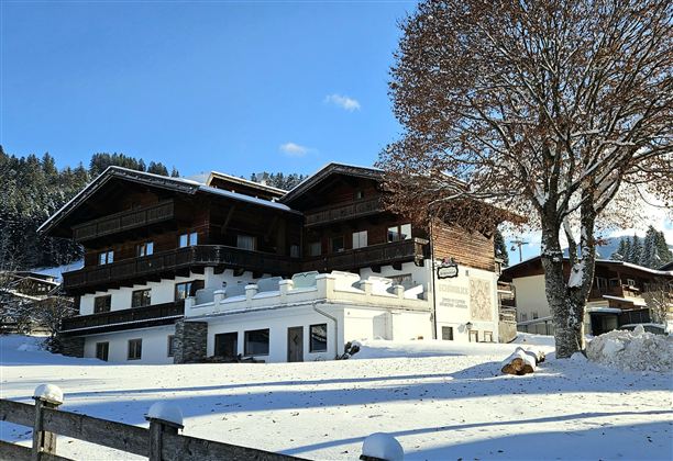 Ein charmantes Holzhaus im Winter, umgeben von schneebedeckten Landschaften. Der klare blaue Himmel ergänzt die ruhige, idyllische Atmosphäre.