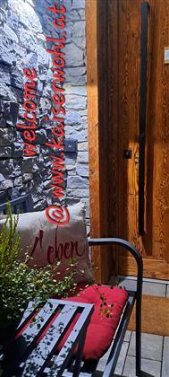 An inviting entrance with wooden cladding and a cozy bench. On the bench lies a cushion with the inscription "Life."