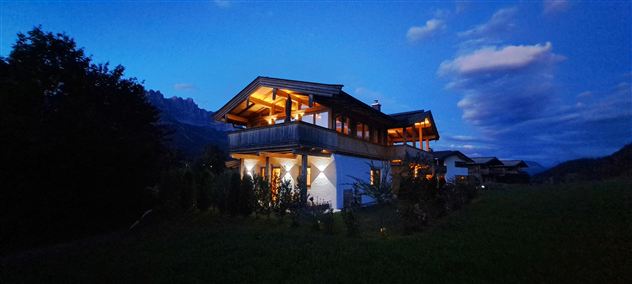 A beautiful house in the evening light, surrounded by greenery. The sky has a gentle twilight with some clouds.