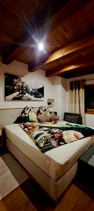 A cozy bedroom with a large bed and wooden ceilings.  
A decorative picture hangs on the wall, and the decor is modern and inviting.