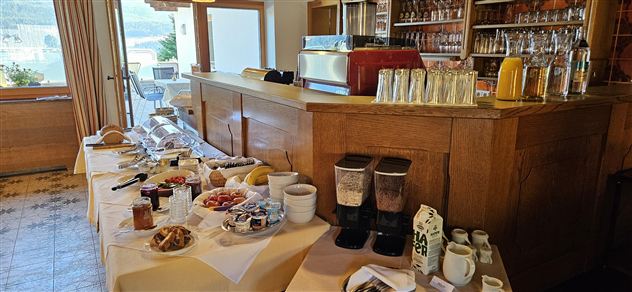 Een uitgebreid ontbijtbuffet met verschillende gerechten en dranken. Op de achtergrond is een uitnodigende barruimte te zien.