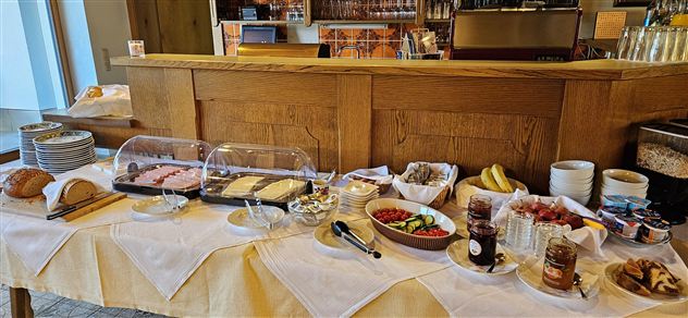 Een uitgebreid ontbijtbuffet met vers brood, vleeswaren, fruit en jam. De tafel is netjes gedekt en uitnodigend.