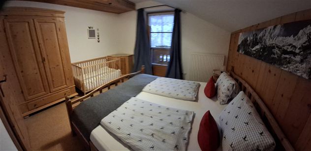 Ein gemütliches Schlafzimmer mit einem Doppelbett und einem Babybett. Die Wände sind aus Holz und das Zimmer hat große Fenster mit Vorhängen.