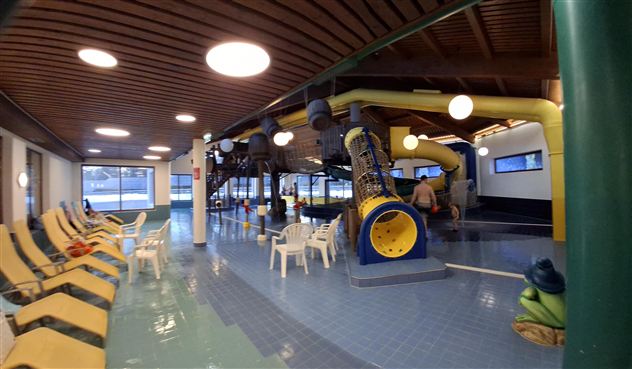 Ein indoor Schwimmbad mit Wasserrutschen und Liegen. Der Raum ist hell und modern gestaltet.