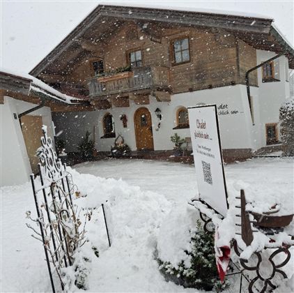 A charming, well-built house in alpine style, surrounded by snow. The snow-covered garden and the wintery ambiance give the picture a tranquil atmosphere.
