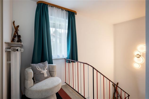An inviting hallway with a cozy seating area and a window. The walls are light, and the space is accented by a modern lamp and beautiful curtains.