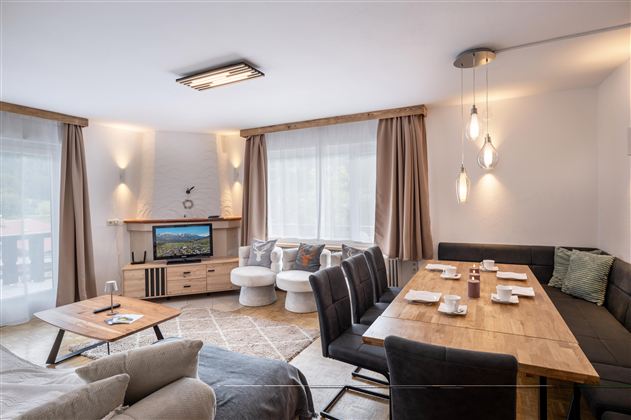 A modern living room with a large dining table and comfortable seating. 

Large windows let in plenty of light and create a cozy atmosphere.