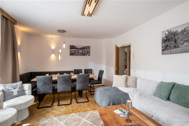 A modern living room with a cozy couch and a dining table for twelve people. The walls are painted light and a large window ensures plenty of light.