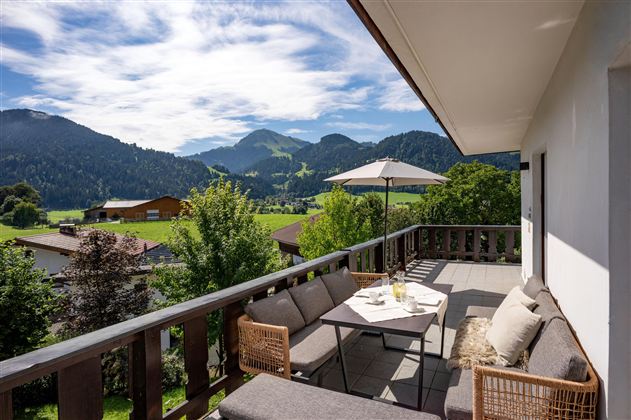 A beautiful terrace with comfortable furniture and a magnificent view of green mountains. The sky is clear and the landscape is idyllic.