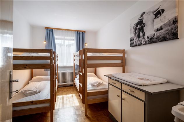 A simple bedroom with two bunk beds and a wardrobe. On the wall hangs a picture of cows.