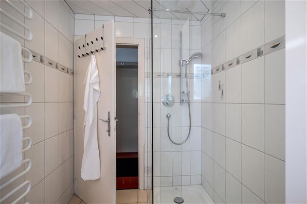 A modern bathroom with a glass shower. White tiles and a towel rack complete the furnishings.