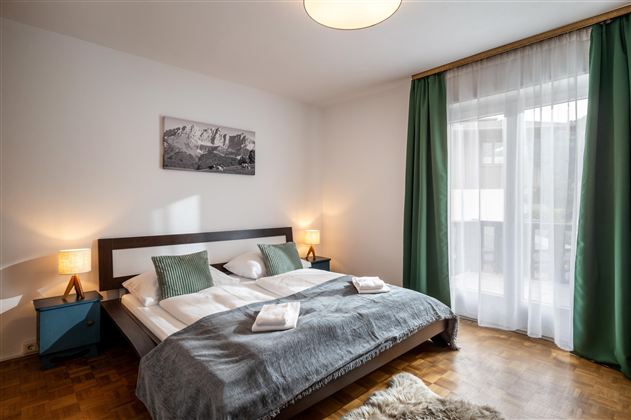 A modern bedroom with a large bed and soft colors. Windows with curtains let in plenty of light and create an inviting atmosphere.