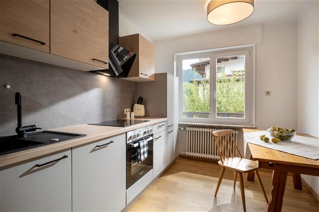 Modern kitchen with wooden and white elements. A table with fruit and large windows creates a bright, welcoming atmosphere.