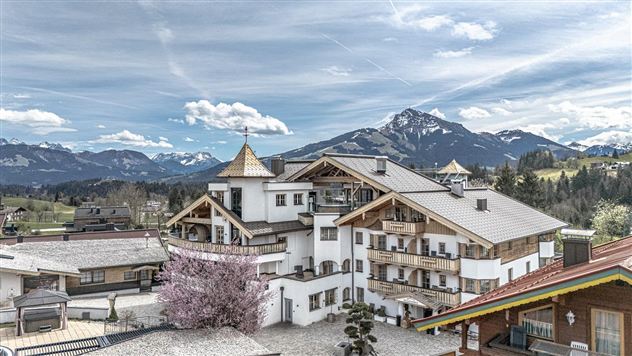 Ein schönes Gebäude in einer malerischen Berglandschaft. Im Hintergrund sieht man die Berge und einen klaren Himmel mit Wolken.