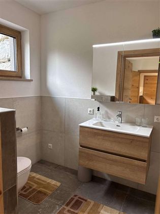 Ein modernes Badezimmer mit einem Waschbecken und einem großen Spiegel. Es hat helle Wände und einen Holzlook, der eine angenehme Atmosphäre schafft.