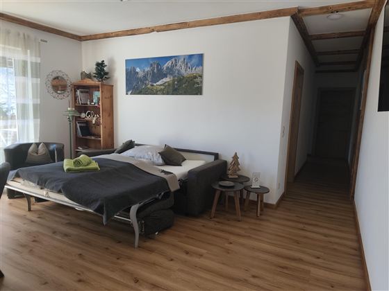 Een gezellige kamer met een bed en een bank. Aan de muur hangt een landschapsschilderij, en de ruimte heeft een houten vloer en lichte muren.