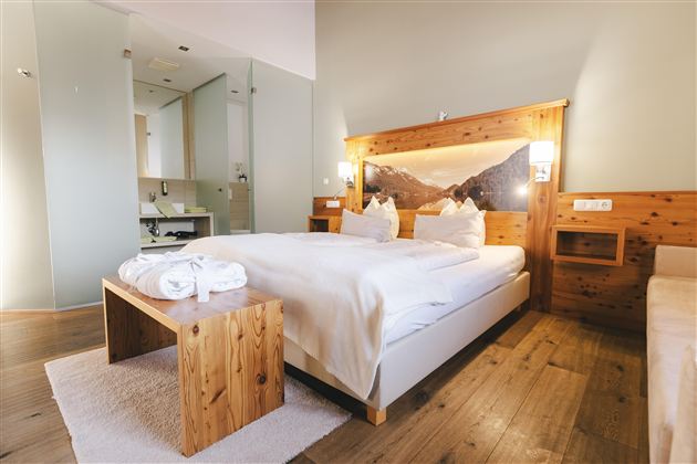 Ein gemütliches Zimmer mit einem großen Bett und Holzdetails. Das helle Ambiente schafft eine entspannende Atmosphäre.