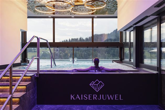 Ein modern gestalteter Wellnessbereich mit einem Pool und großen Fenstern. Im Vordergrund entspannt eine Person im Wasser.