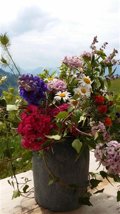 Ein schöner Strauß mit bunten Blumen in einer grauen Vase. Die Blumen sind frisch und leuchtend, vor einem natürlichen Hintergrund.