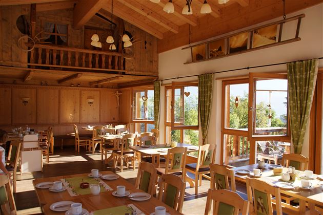 Een gezellig restaurant met houten decor en grote ramen. Er zijn tafels met gedekte borden en een uitnodigende sfeer.