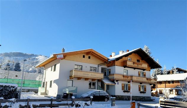 Eine malerische Winterlandschaft mit zwei charmanten Häusern, die von Schnee bedeckt sind. Der klare Himmel und die umliegenden Berge schaffen eine ruhige Atmosphäre.