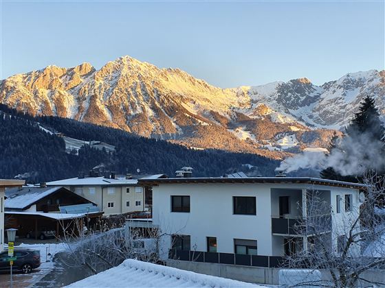 A picturesque winter landscape with snow-covered mountains in the background. In the foreground stands a modern residential house.