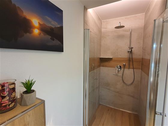 Ein modernes Badezimmer mit einer Dusche und eleganten Fliesen. An der Wand hängt ein Bild einer Landschaft mit Sonnenuntergang.