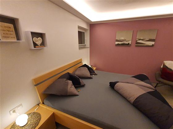 Ein stilvolles Schlafzimmer mit einem Doppelbett und dekorativen Kissen. Die Wände sind in sanften Farben gehalten, mit Bildern und modernen Regalen.