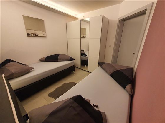 Ein einfaches Schlafzimmer mit zwei Einzelbetten und einem modernen Kleiderschrank. Die Wände sind in sanften Farben gestrichen, und es gibt ein Bild an der Wand.