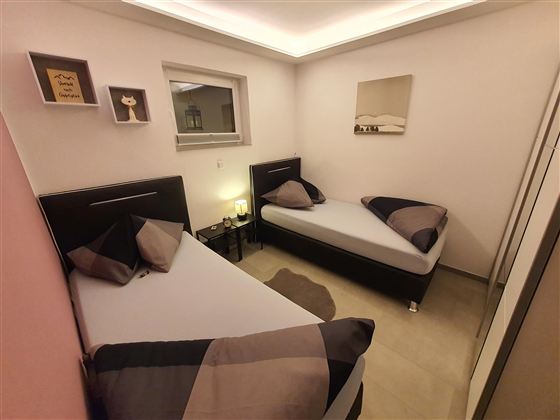 Ein kleines, modernes Zimmer mit zwei Einzelbetten und eleganter Dekoration. Die Wände sind in neutralen Farben gehalten, und es gibt einen Nachttisch mit einer Lampe.