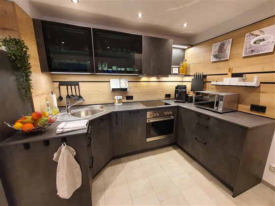 Moderne Küche mit dunklen Schränken und hellen Wänden. Auf der Arbeitsfläche stehen Küchenutensilien und frisches Obst.