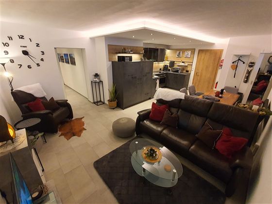 Ein gemütliches Wohnzimmer mit einer großen Ledercouch und dekorativen Kissen. Die offene Küche ist modern und gut ausgestattet, mit einem warmen Ambiente.