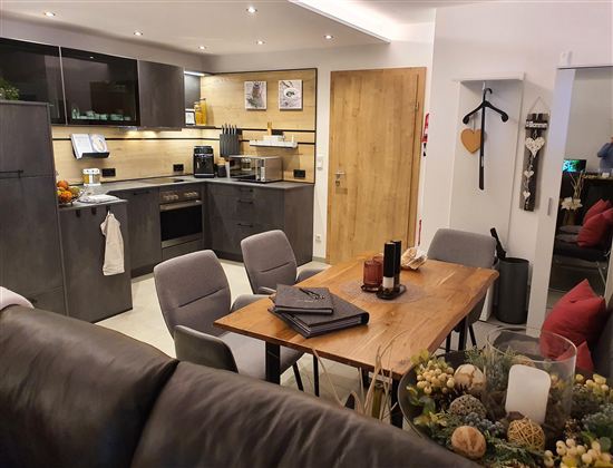 Moderne Küche mit einem Esstisch und Stühlen. Das Design ist schlicht und elegant, mit warmen Farben und gut angeordneten Möbeln.