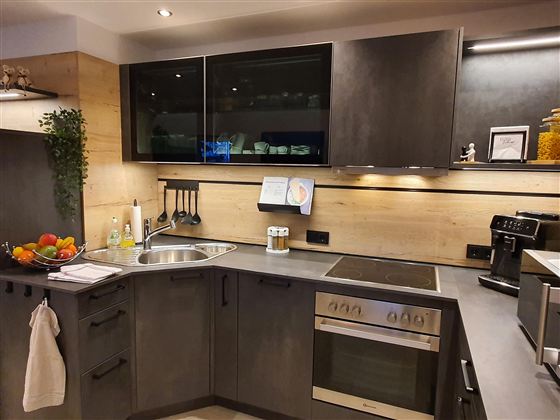 Eine moderne Küche mit dunklen Möbeln und Holzakzenten. Der Raum ist gut beleuchtet und enthält eine Spüle, einen Herd und frisches Obst auf der Arbeitsplatte.