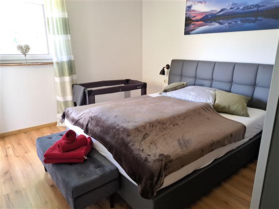 Een moderne slaapkamer met een groot bed en een gezellige dekbed. Een stoel en een tafel vullen de eenvoudige, elegante inrichting aan.