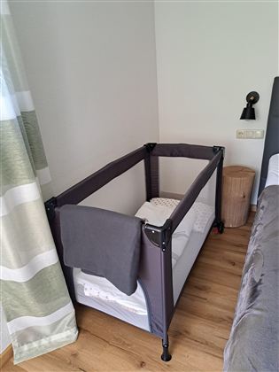 Een kinderbed in een moderne slaapkamer. Het bed is uitgerust met een deken en staat naast een bed en een nachtkastje.