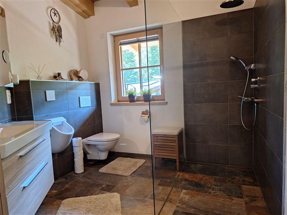 Een moderne badkamer met een glazen douche en stijlvolle tegels. Het heeft een wastafel, een toilet en een raam met natuurlijk licht.