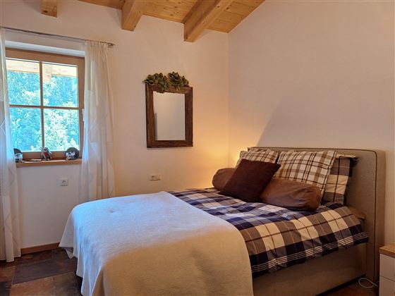 Een gezellige slaapkamer met een tweepersoonsbed, een raam en een houten frame. De inrichting is warm en uitnodigend, met een zachte tint.