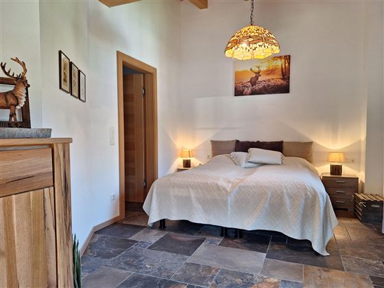 Een gezellige slaapkamer met een groot bed en een elegante kroonluchter. Aan de wand hangt een afbeelding van een hert, en de vloer is van stenen.