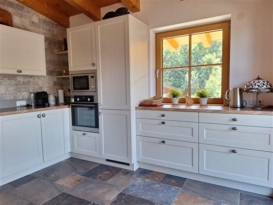 Een moderne keuken met witte kasten en een groot raam. Het werkblad is keurig uitgerust met enkele keukenaccessoires en decoratieve planten.