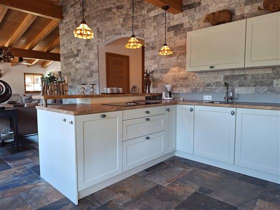 Een moderne keuken met witte kasten en houtwerk. De vloer bestaat uit donkere tegels en de verlichting creëert een gezellige sfeer.