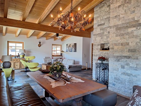 Een gezellige woonkamer met houten plafonds en een grote eettafel. De inrichting is modern met rustieke elementen en een mooie steenwand.