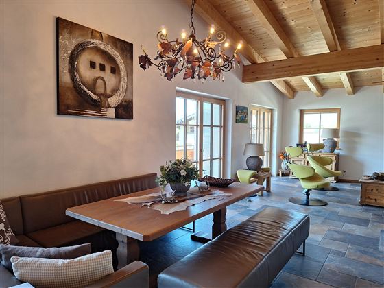 Een uitnodigende eetkamer met een grote houten tafel en gezellige zitplaatsen. De ruimte heeft lichte muren, houten plafonds en een moderne kroonluchter.