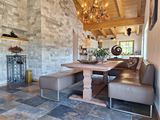 Een moderne eetkamer met een grote houten tafel en stijlvolle banken. De wanden zijn bekleed met stenen, en een mooie plafondlamp hangt boven de tafel.